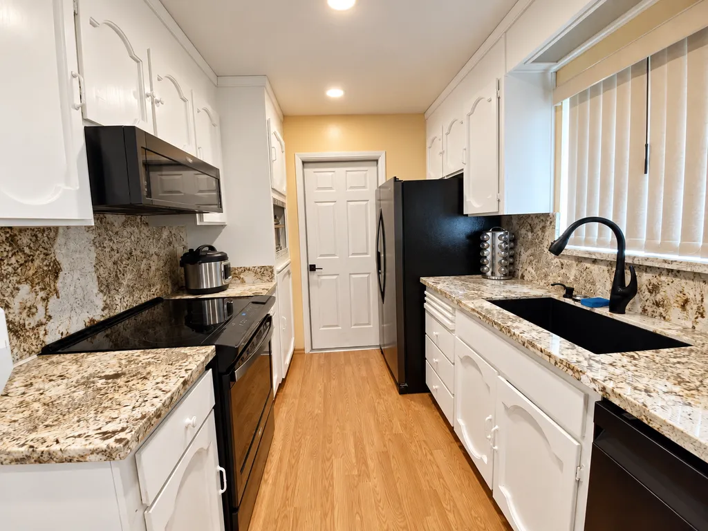 A kitchen with white cabinets, granite countertops, black appliances, and a wooden floor.