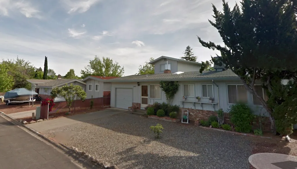 A white house with a driveway, garage, and plants in front.