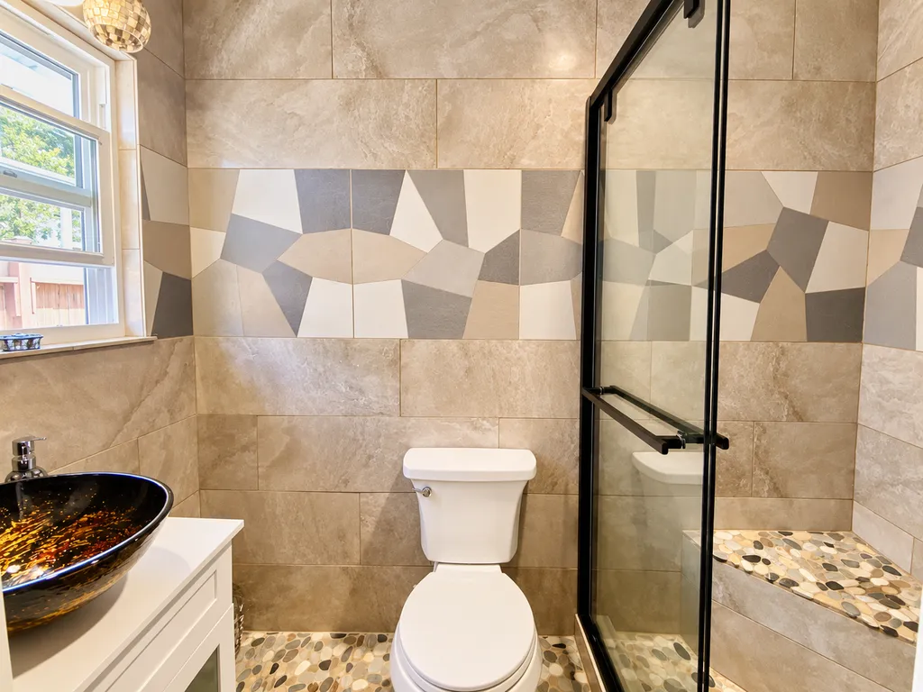A bathroom with a white toilet, a glass shower door, and a patterned tile wall.