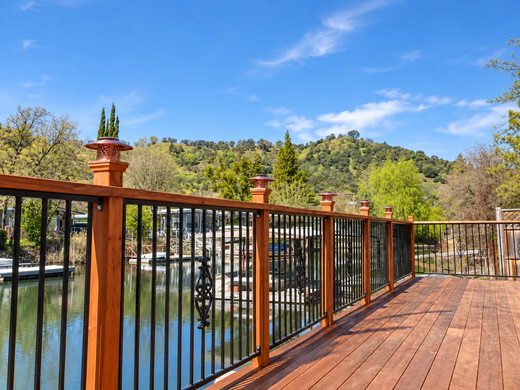A wooden deck with black railings overlooking a calm lake with hills in the distance.