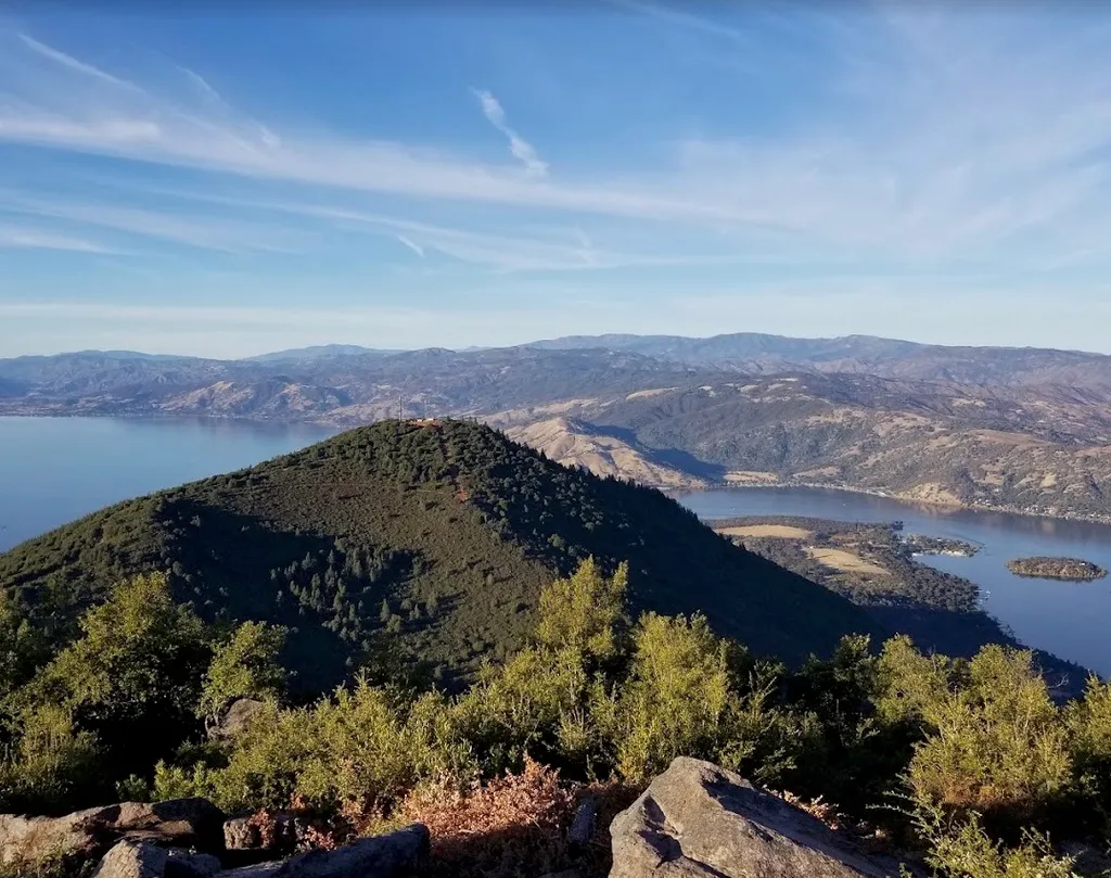 Mountaintop view with a lake and distant hills under a blue sky.